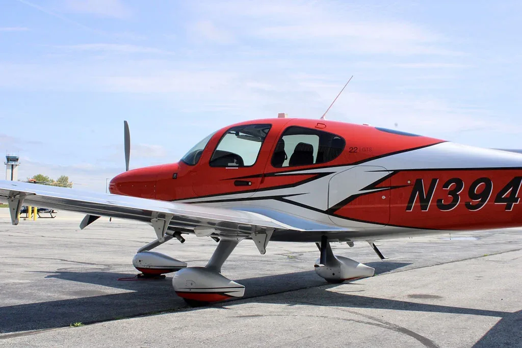 A close-up side view of a red and silver Cirrus SR22 GTS aircraft with registration N394JM parked on an airfield.