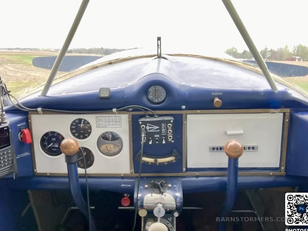 The blue instrument panel and controls of a vintage Piper aircraft, with a view of a field through the windshield.