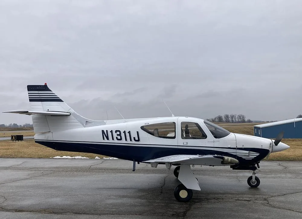 A side view of the white and blue single-engine aircraft N1311J parked on a wet tarmac.