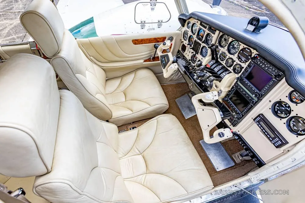 The cream-colored leather pilot and co-pilot seats of an aircraft, with a partial view of the instrument panel and side panel.