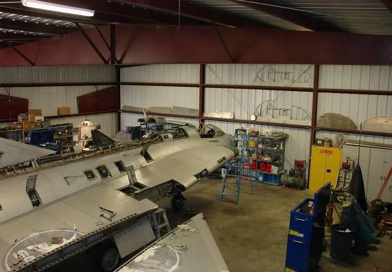 An overhead view of a disassembled Saab Draken aircraft undergoing restoration in a hangar.