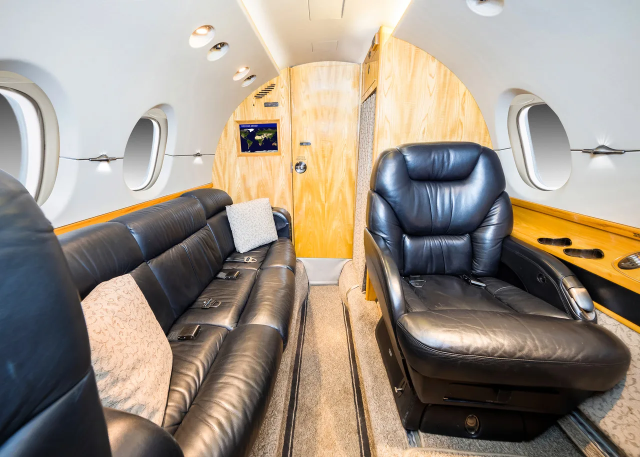 The spacious interior of a private jet featuring a black leather sofa and a single executive seat.