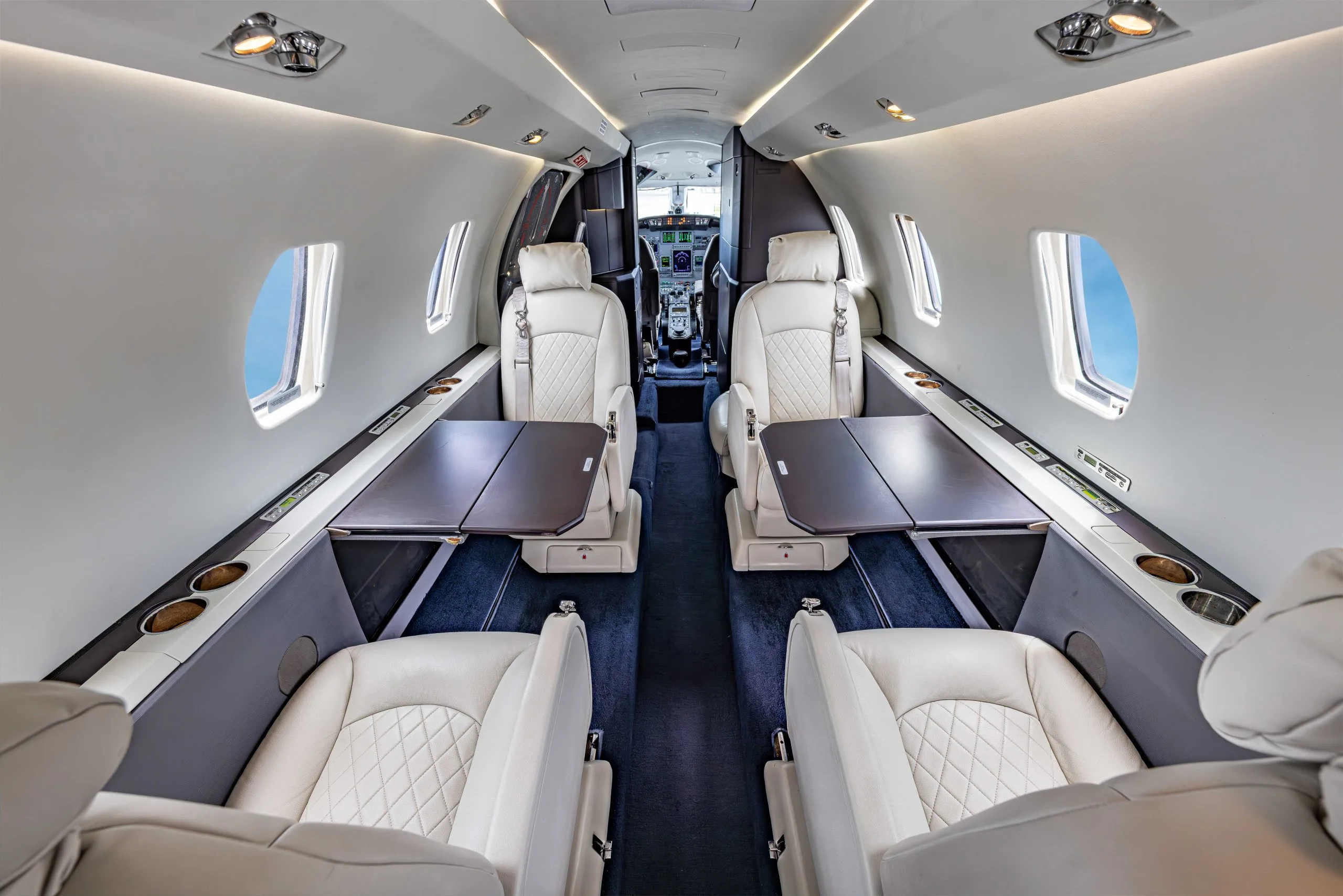 Forward view of the aircraft's interior with white leather seats and dark wood tables.