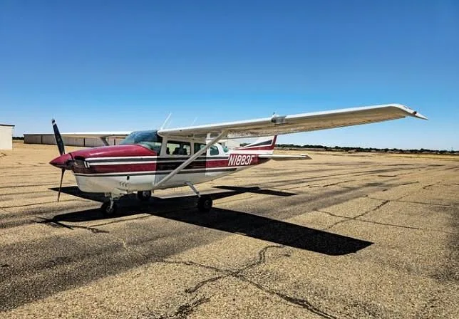 A white and maroon Cessna 210 Centurion aircraft with registration N1883F parked on an asphalt runway under a clear blue sky.