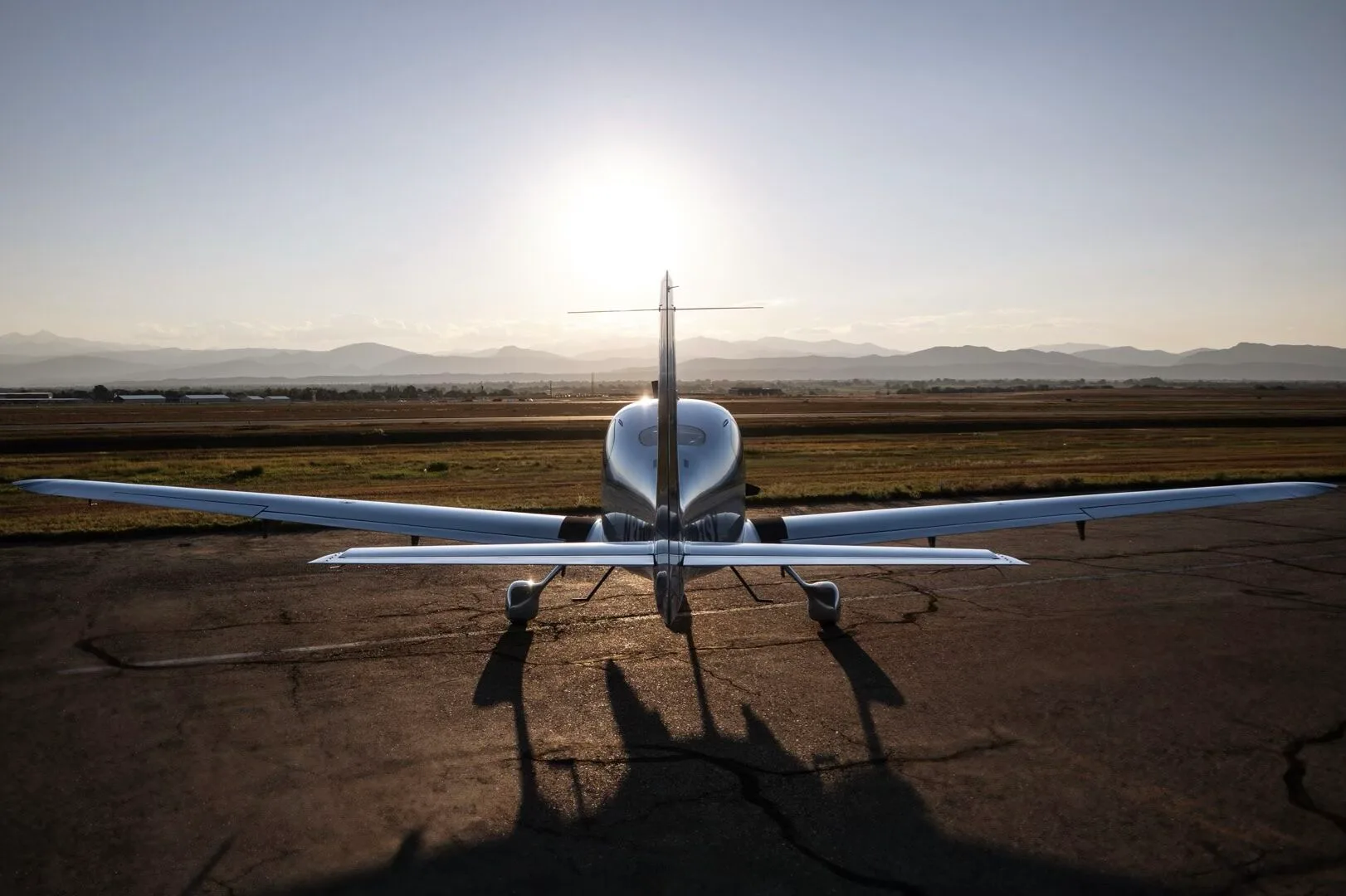 Rear view of a Cirrus SR22T aircraft, N31SX, on an airfield with the sun setting behind it.
