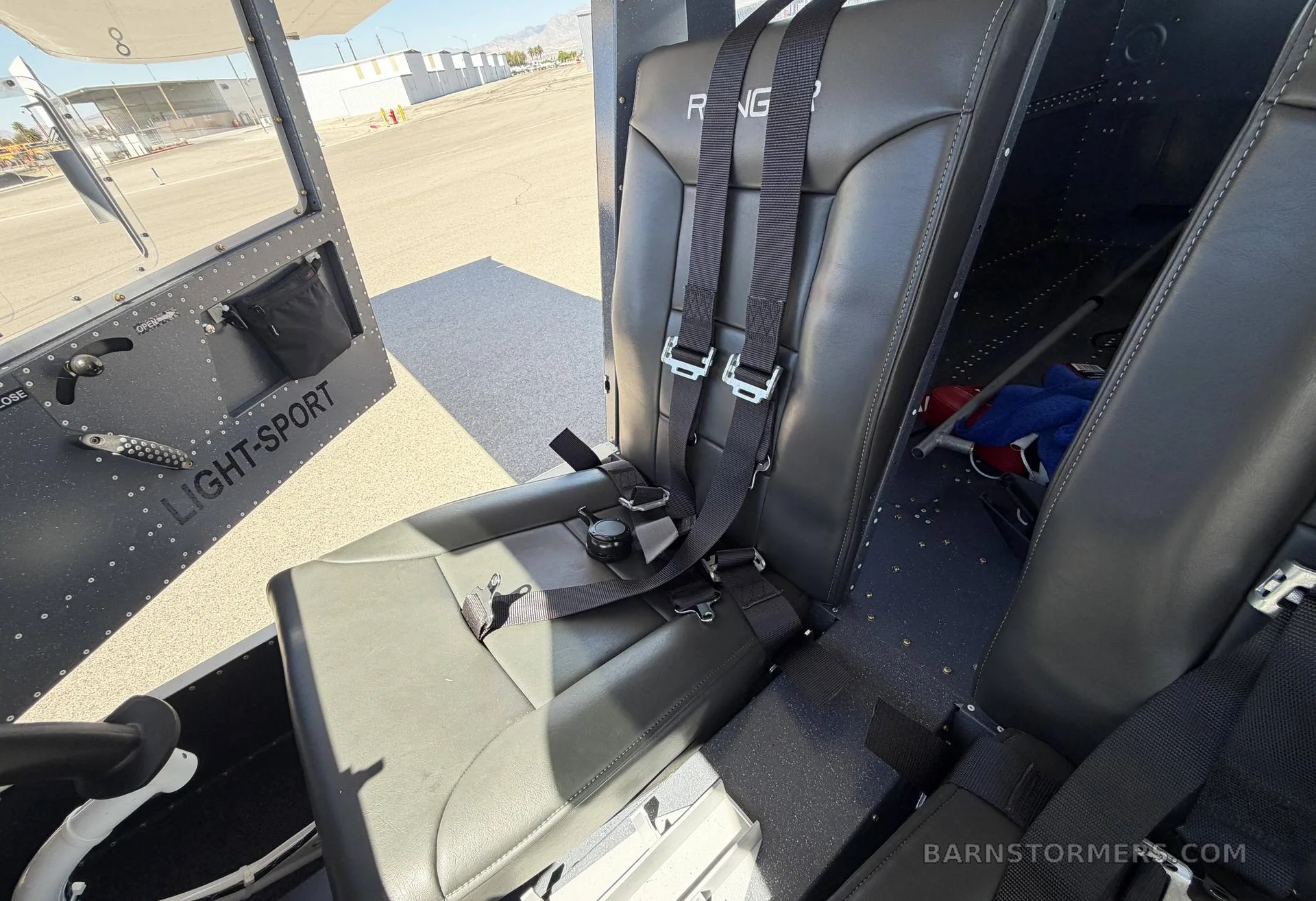 The interior cabin of a 'Ranger' light-sport aircraft, showing two black seats with harnesses and the 'LIGHT-SPORT' text on the side panel.