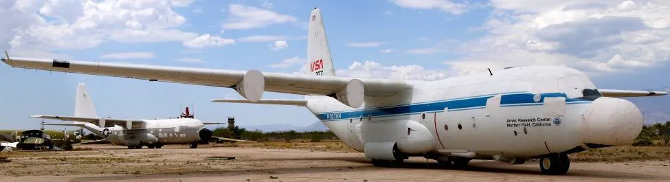 A white NASA C-130 aircraft with covered nose and engines is parked in a desert boneyard.