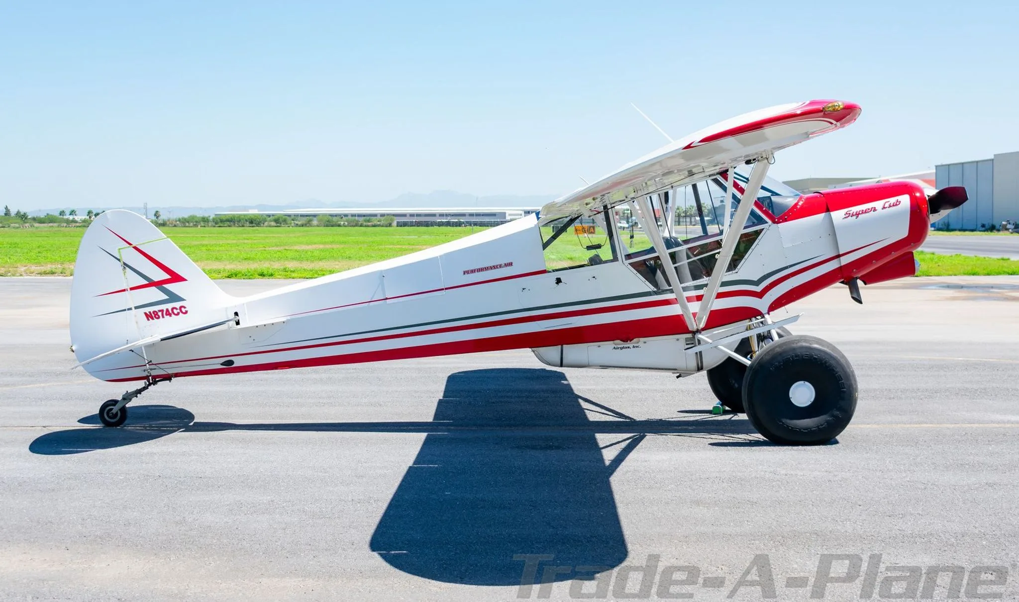 A side view of a red and white Super Cub aircraft with tail number N874CC, parked on an airfield.