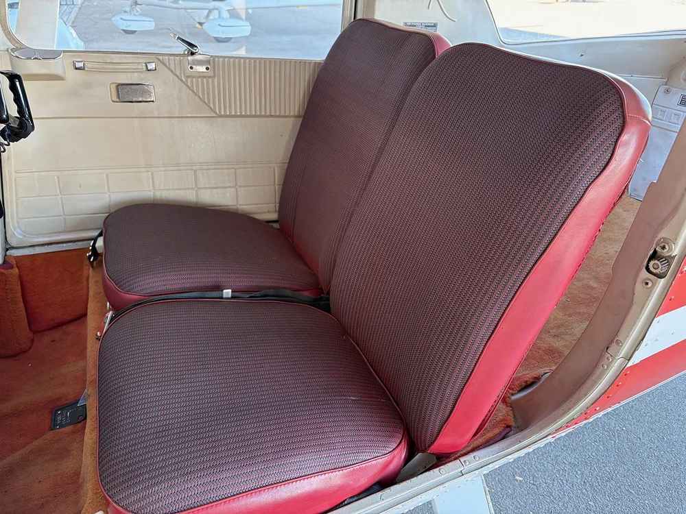 Two red and black patterned aircraft cabin seats in the interior of a small plane.