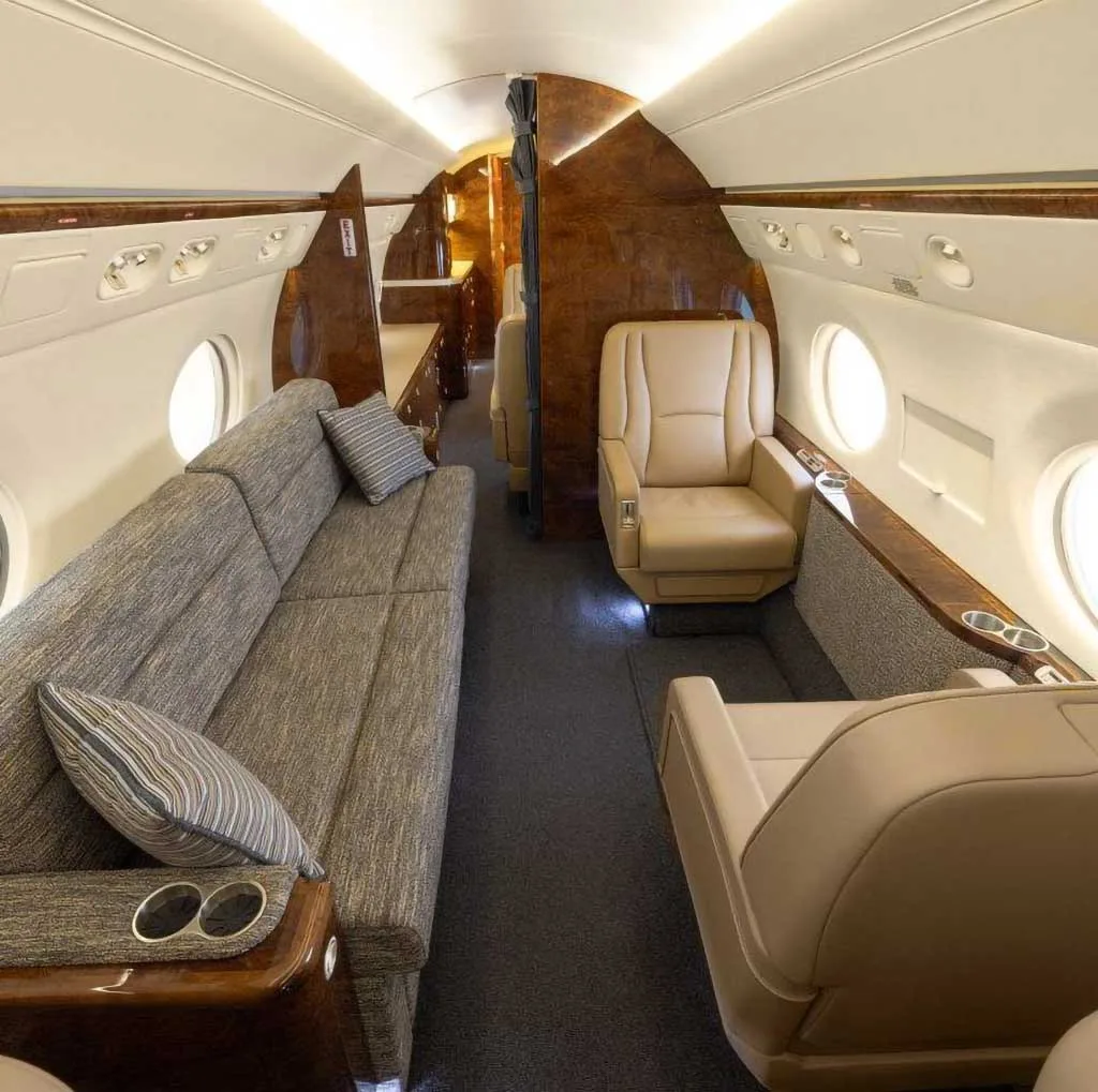 A view of the business jet's cabin interior showing a long sofa and individual tan leather seats.