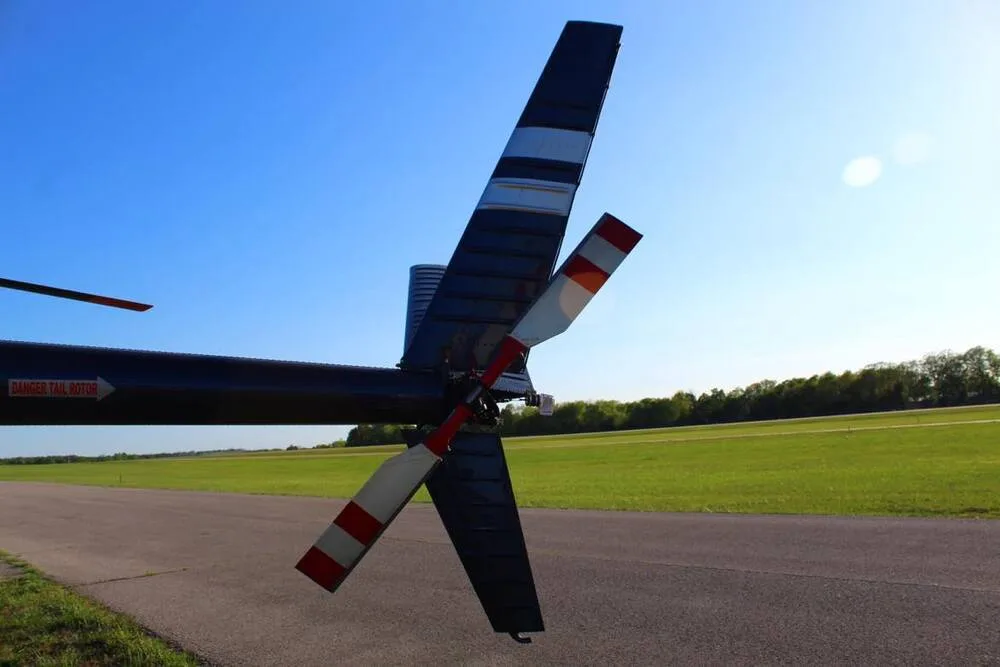 A close-up view of the tail rotor of a blue and white helicopter, showing red and white striped blades and a "DANGER TAIL ROTOR" warning.
