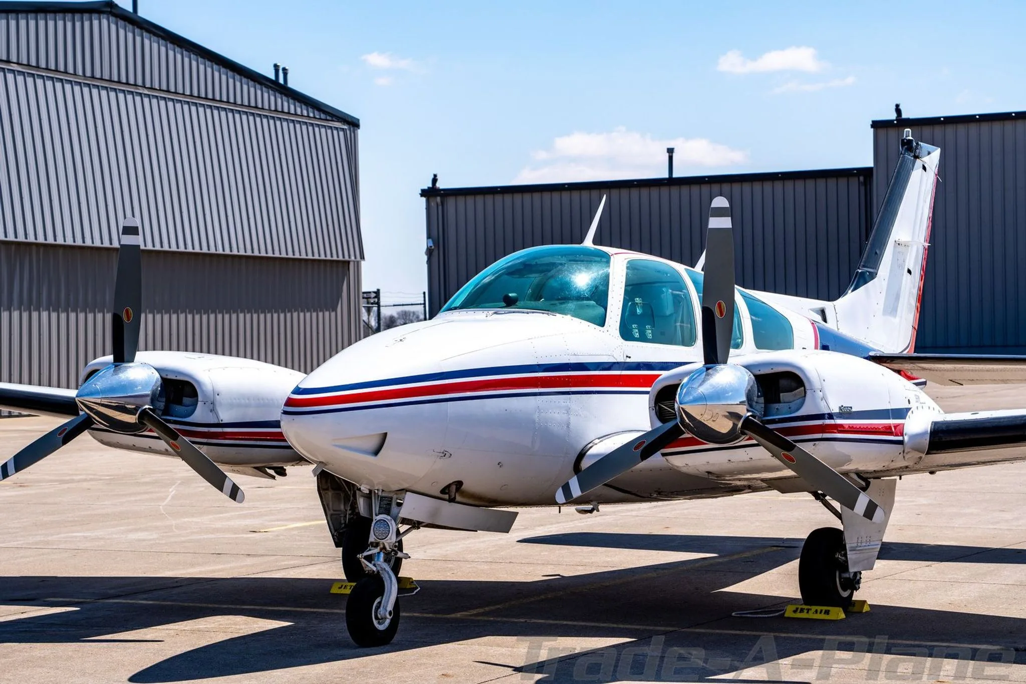 Front-left view of the N4UF twin-engine Beechcraft Baron with red and blue stripes on an airfield.