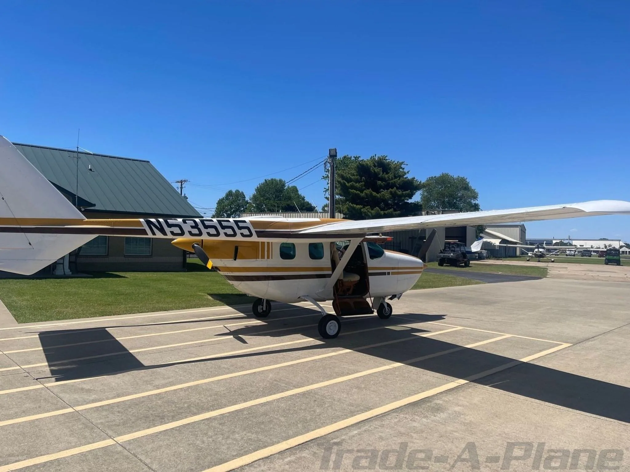 A side view of a white and gold Cessna 206 aircraft with its door open, parked on an airfield.