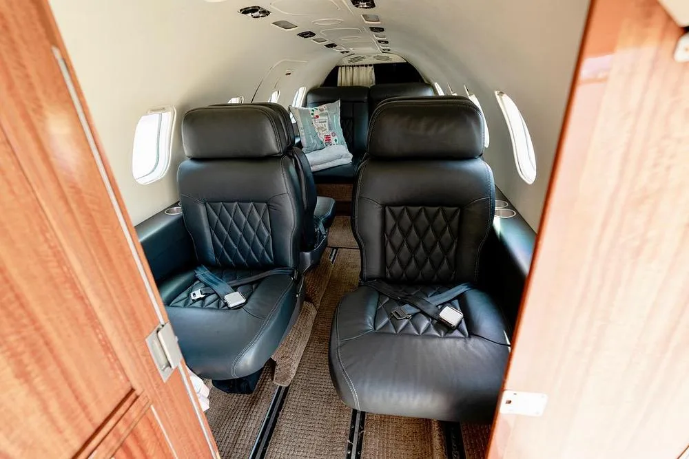 View into the aircraft cabin from the front, showing two black leather seats and a couch further back.