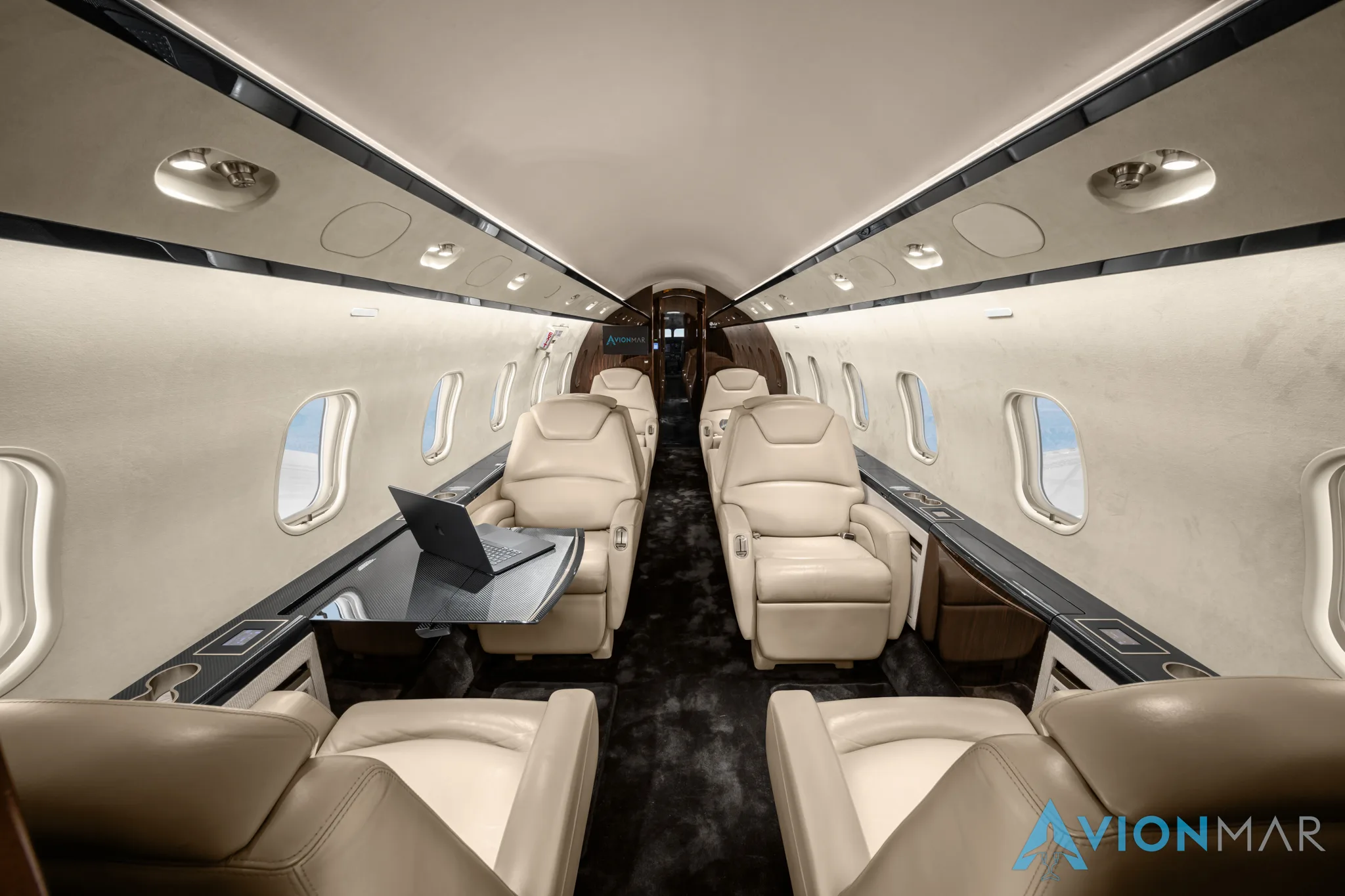 The luxurious interior of a private jet cabin with cream leather seats and a laptop on a table.
