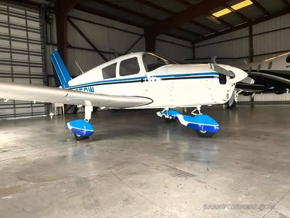 View from inside a light aircraft cabin, showing a grey seat with blue stripes and an airport runway outside.