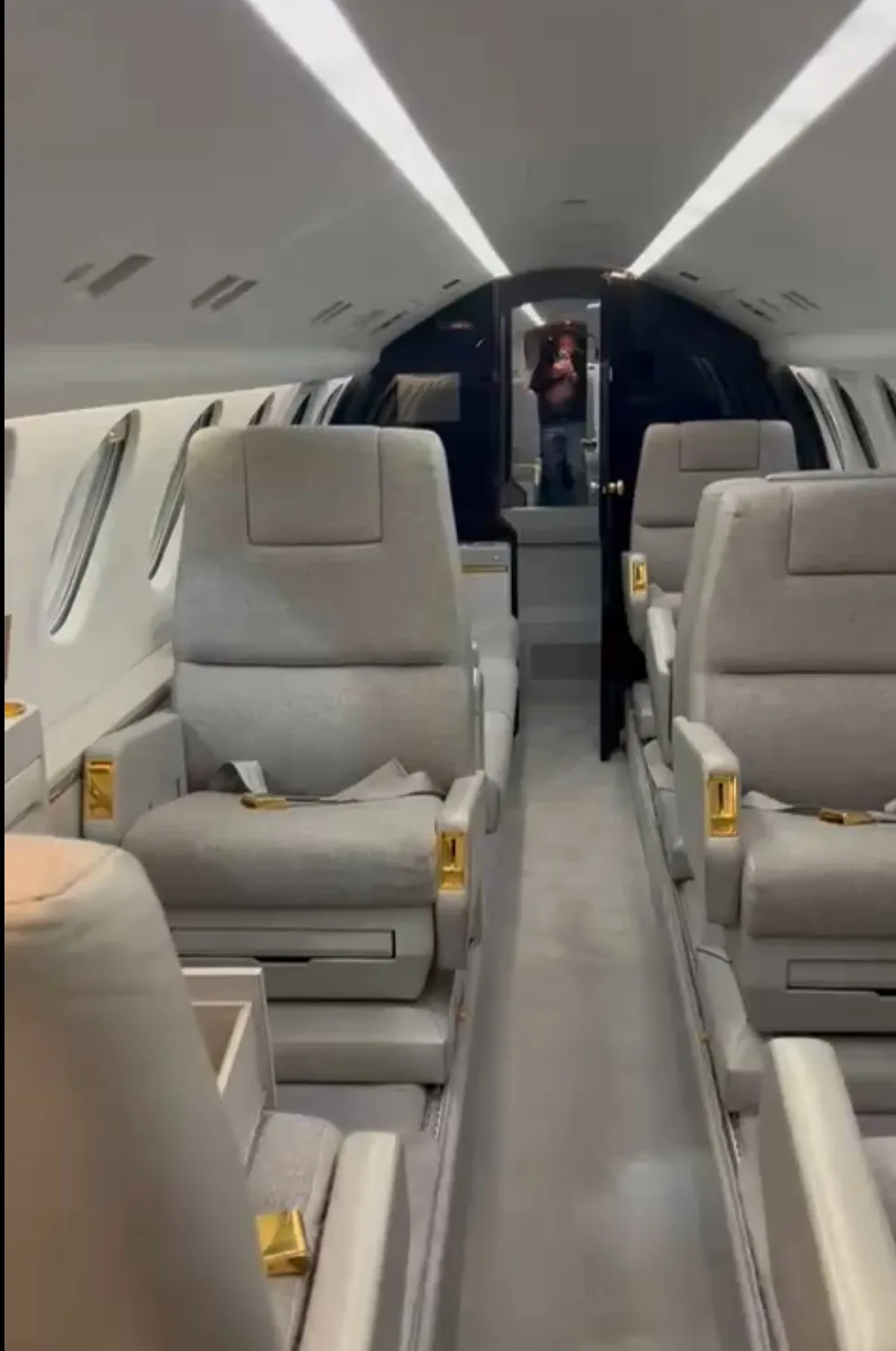 The aircraft's interior cabin with grey seats and gold accents, looking down the aisle.