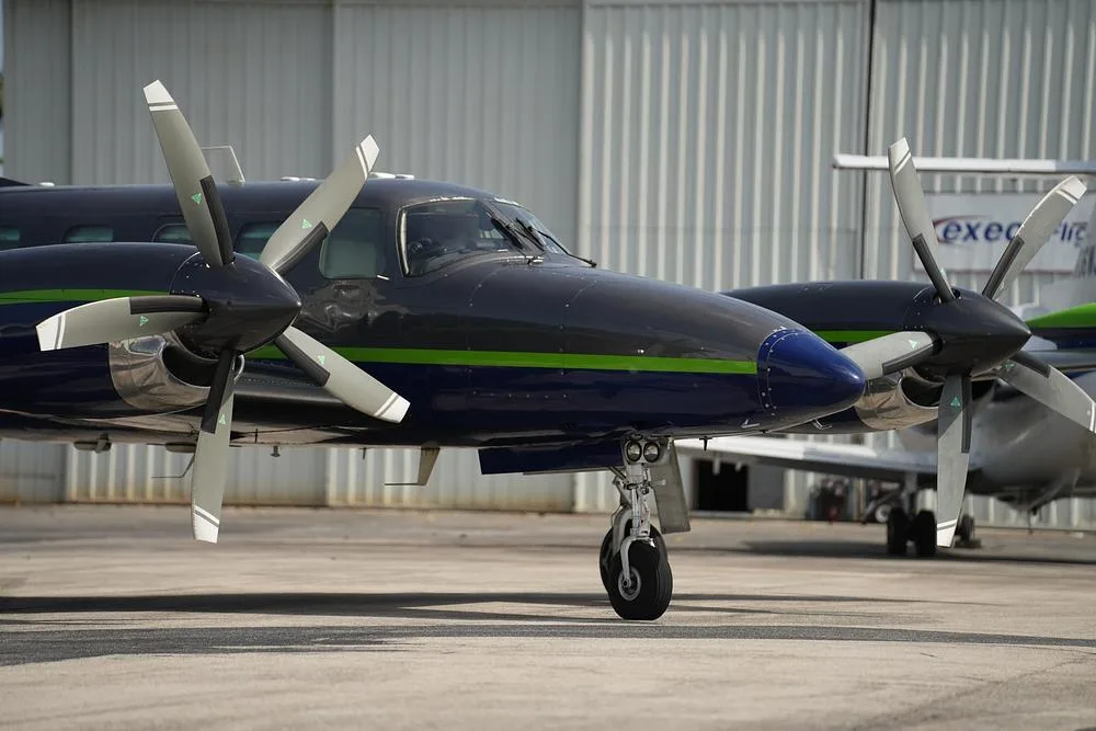 A close-up view of the nose and propellers of a dark blue and grey twin-engine turboprop aircraft.
