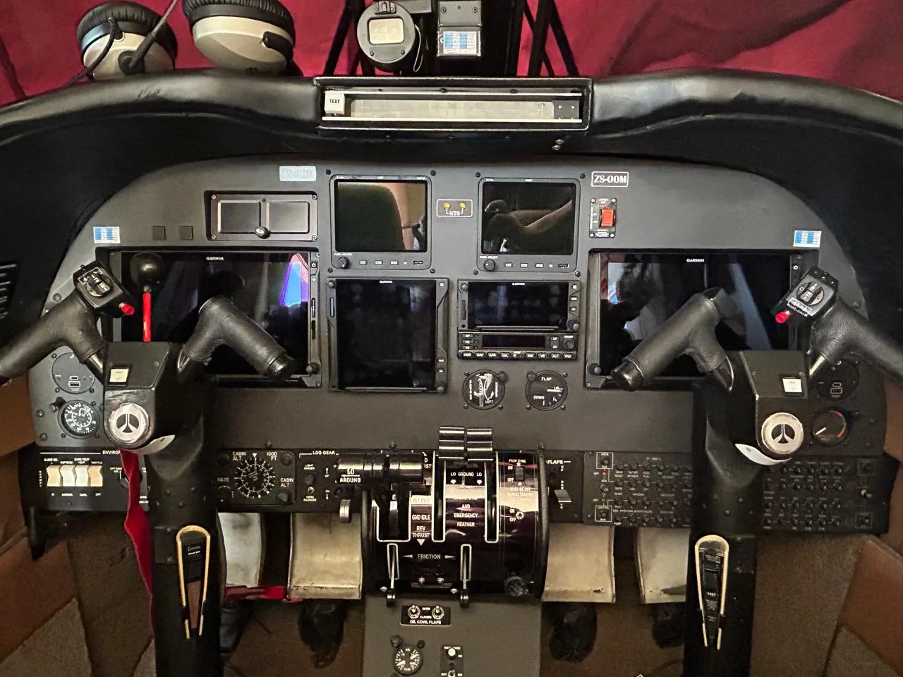The cockpit of a twin-engine aircraft, showing the instrument panel with multiple screens, yokes, and throttle quadrant.