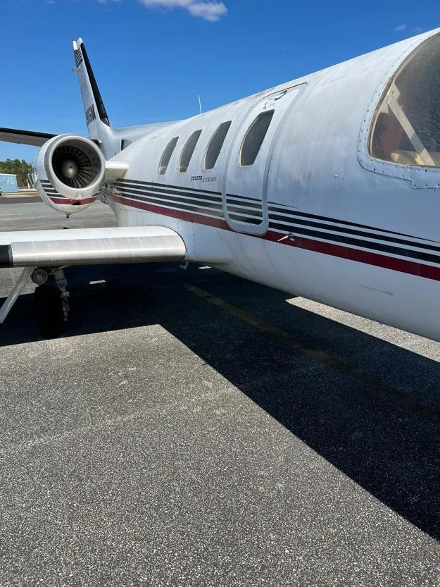 A side view of the fuselage, engine, and wing of a white Cessna Citation I business jet with red and black stripes.