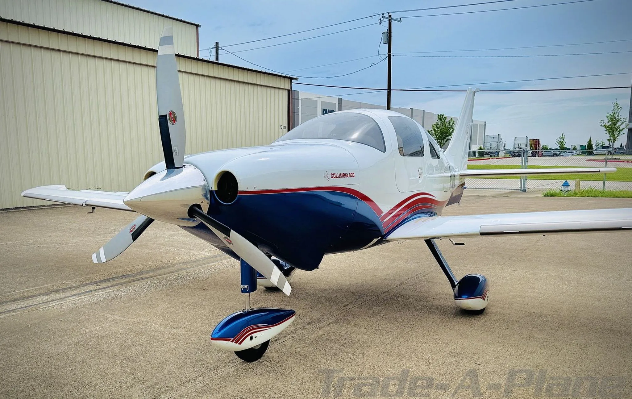 Front-left view of a white and blue Columbia 400 with red stripes on an airport apron.