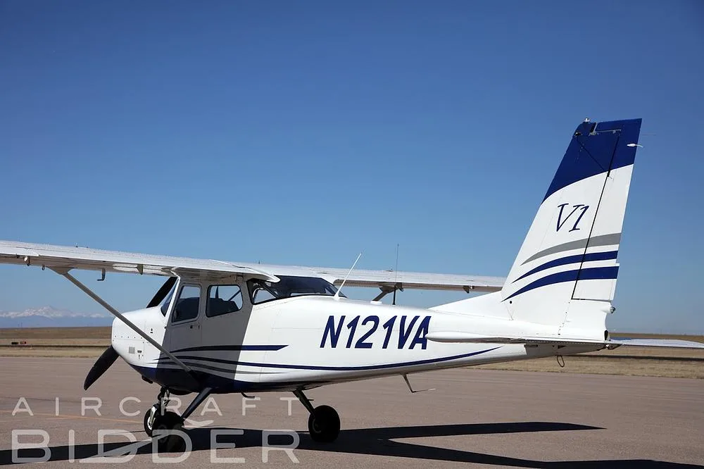 A three-quarter rear view of the white and blue Tecnam P2010 single-engine aircraft, N121VA, on an airfield.