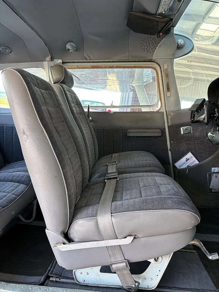 The front cabin seats of an aircraft, upholstered in gray fabric and vinyl, with a view towards the cockpit.