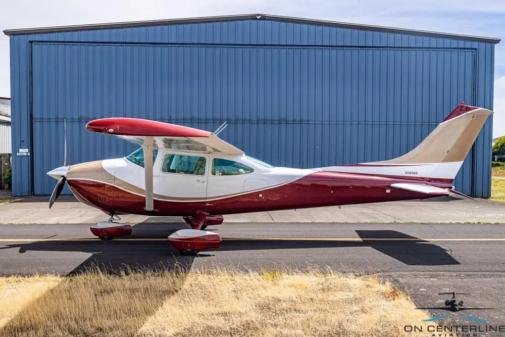 A red, white, and tan single-engine propeller aircraft is parked on an asphalt ramp in front of a blue hangar.