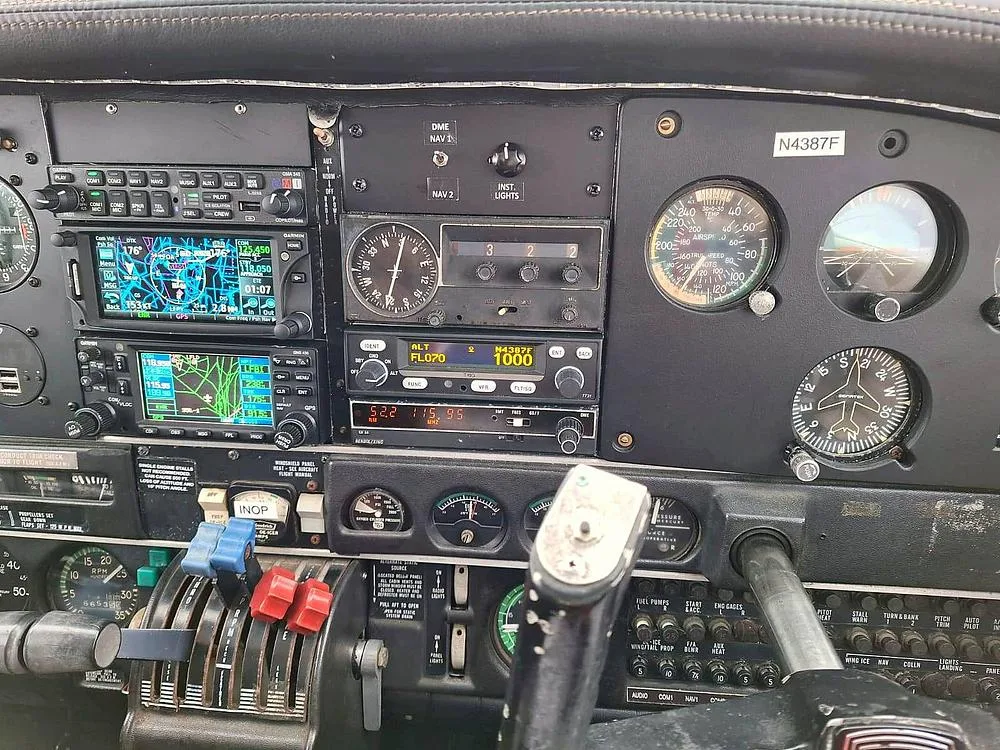 A close-up of the lower section of the cockpit instrument panel of the Piper PA-34 Seneca II, N4387F, showing engine controls and avionics.