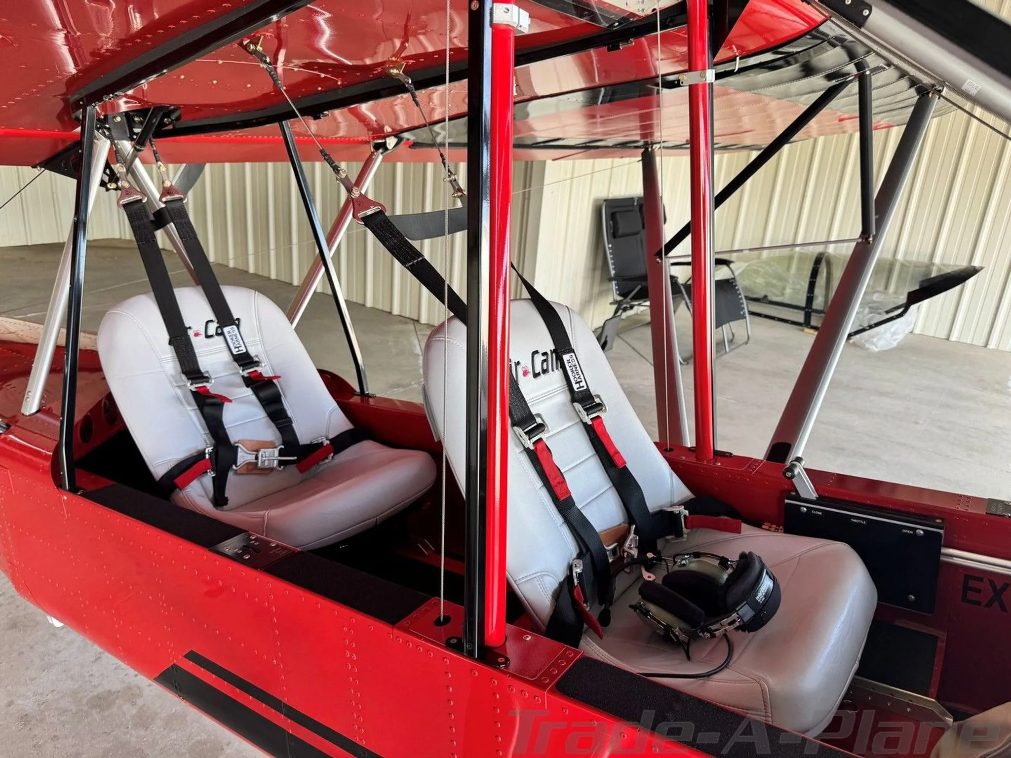 The two white bucket seats with harnesses in the open cockpit of a red Air-Cam aircraft.
