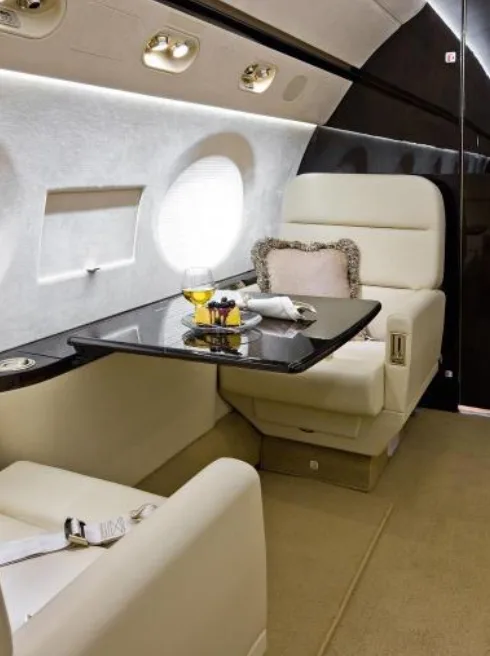 A close-up of a private jet's cream leather seat with a table set with drinks and snacks.