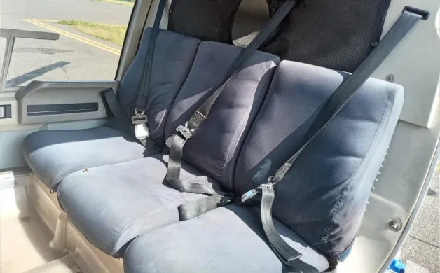 Three dark grey passenger seats with seatbelts are visible in the helicopter's cabin, looking towards the rear.