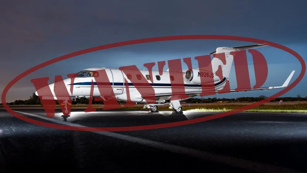 A white business jet with blue stripes, registration N926JS, is parked on a tarmac at night with ground lighting.