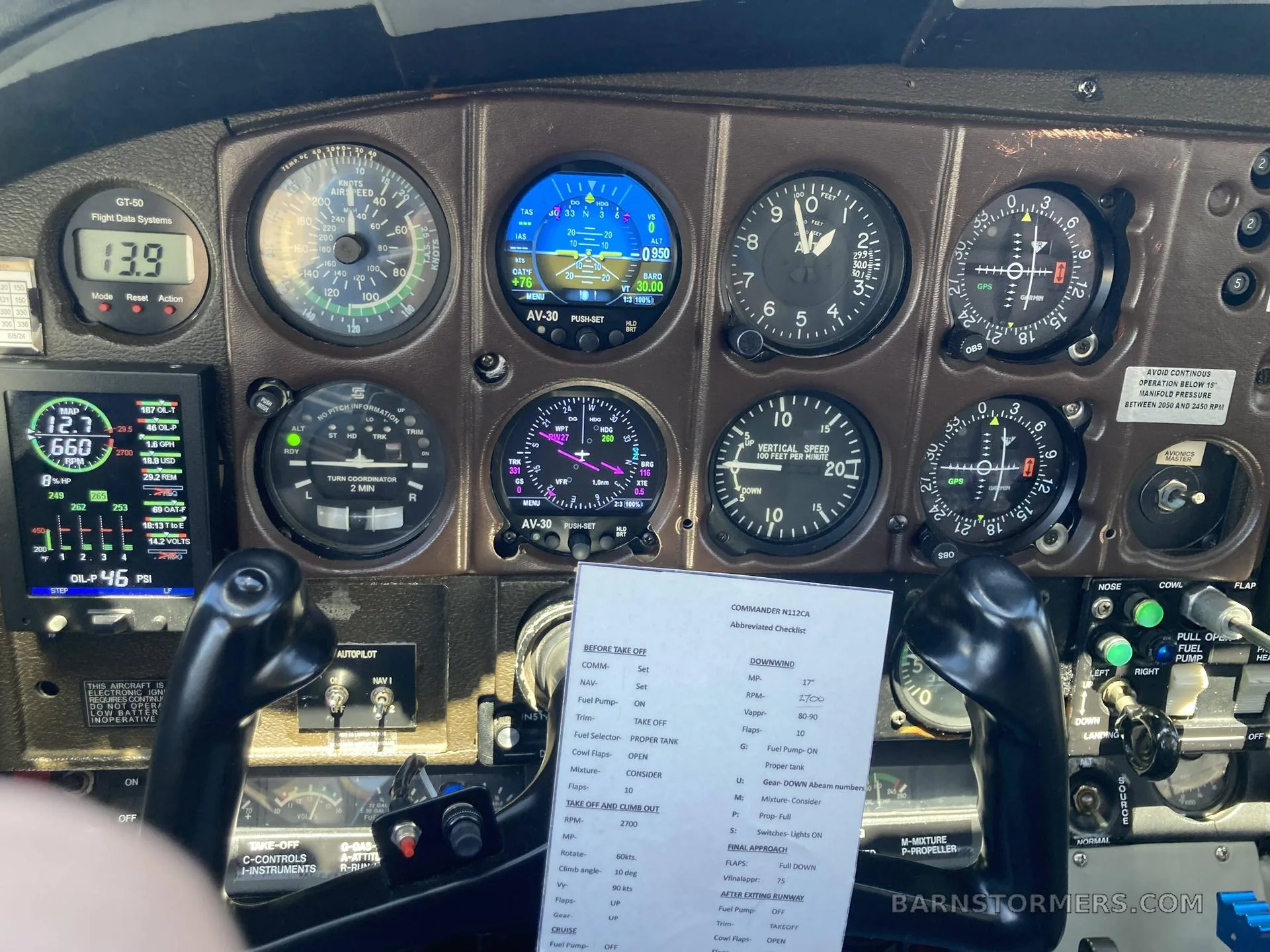 The instrument panel of an aircraft, featuring analog gauges and digital displays, with a checklist on the yoke.