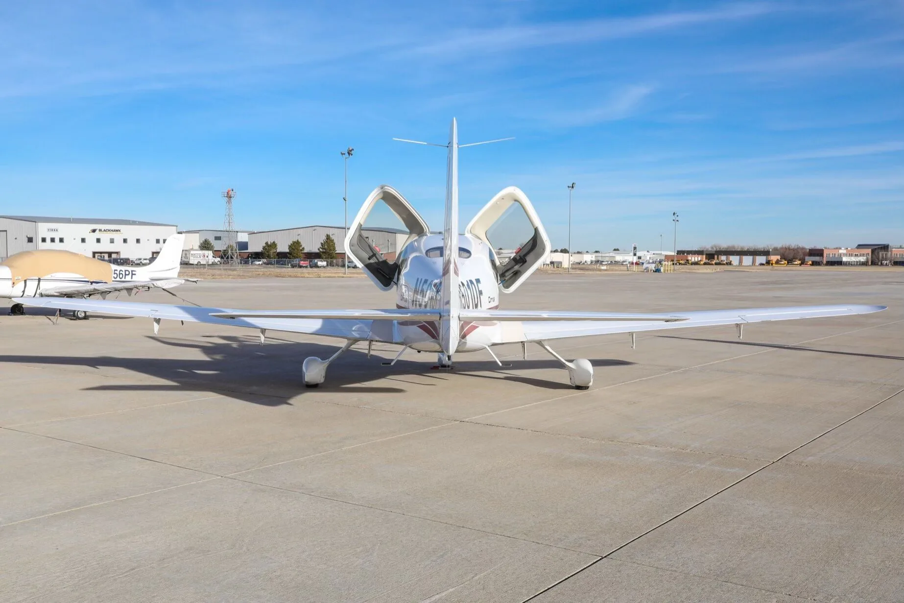 Rear view of a white Cirrus SR20 aircraft with its gull-wing doors open, parked on an airfield.