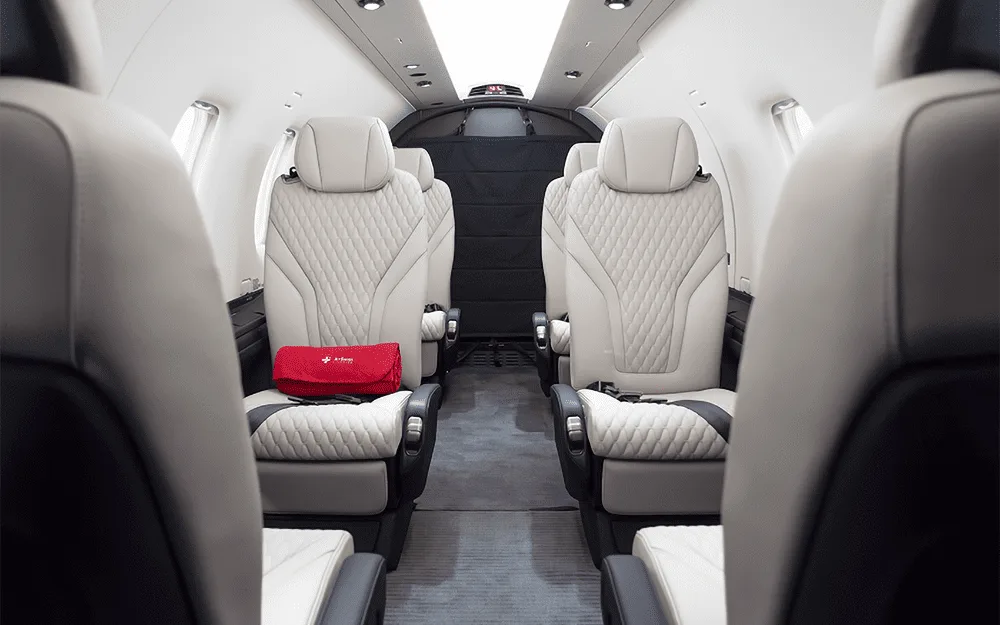 The luxurious white and black quilted leather interior cabin of the Pilatus PC-12 NGX, with a red bag on a seat.