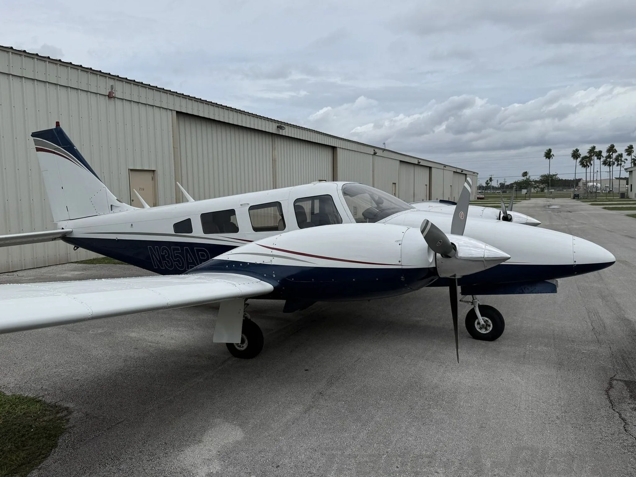 Side view of the white and blue twin-engine propeller aircraft N35AR parked on an asphalt apron next to a hangar.