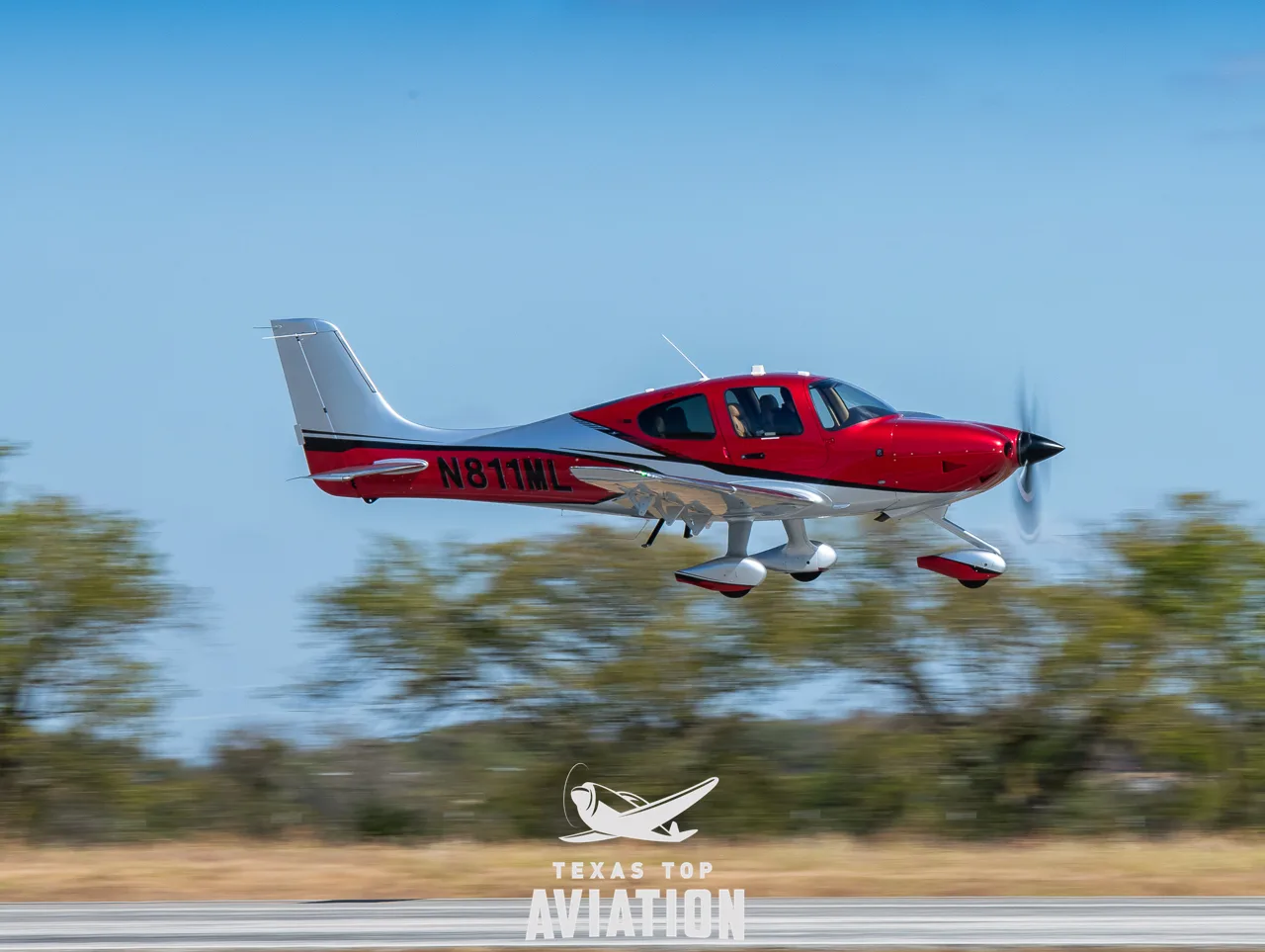 A red and silver Cirrus SR22T GTS aircraft with registration N811ML in flight over a runway.