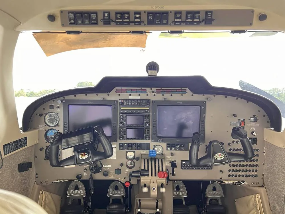 The cockpit of a twin-engine aircraft, showing the instrument panel with two large displays and control yokes.