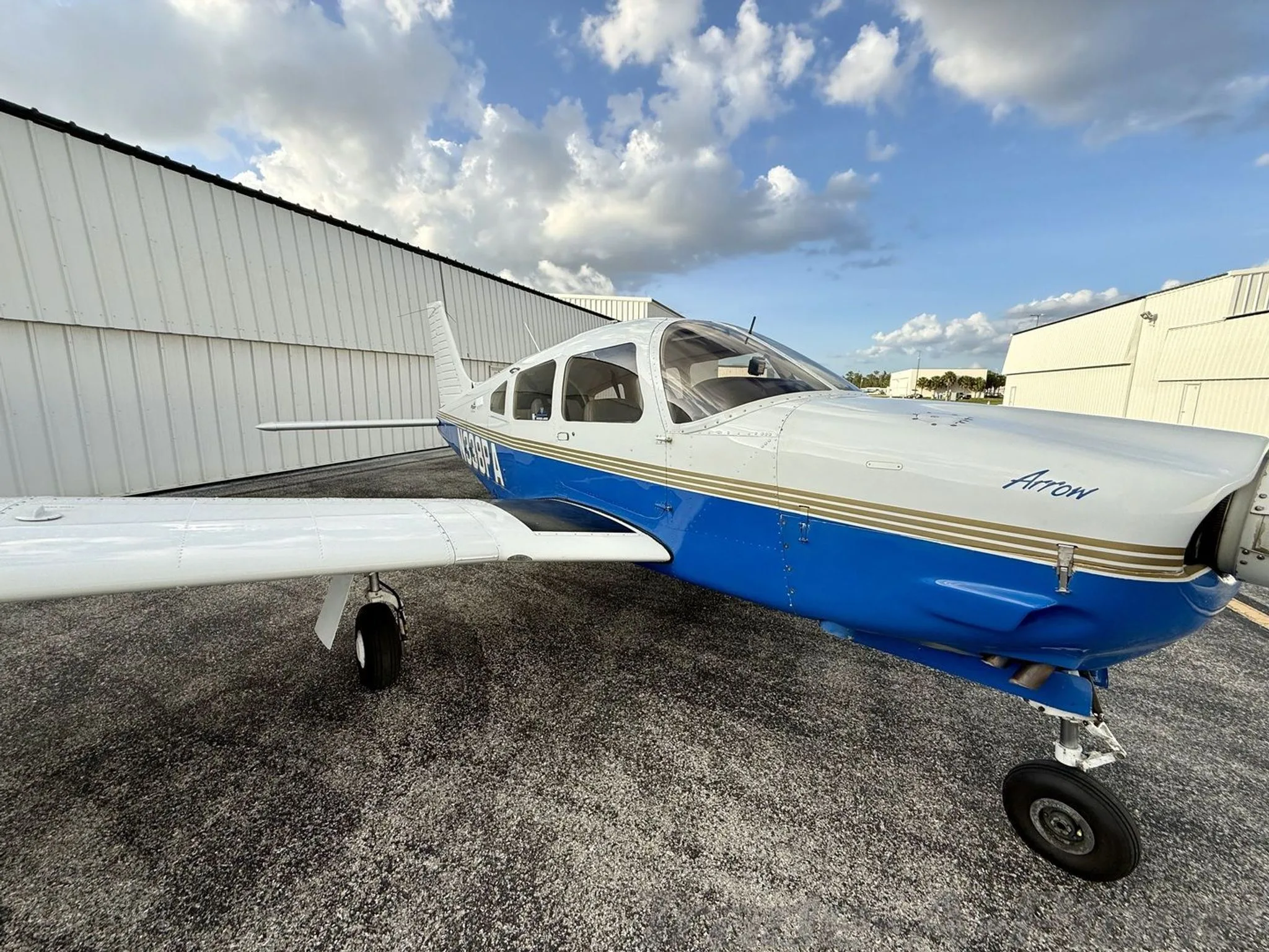 A close-up front-side view of the white and blue Piper Arrow aircraft (N338PA) on the tarmac.
