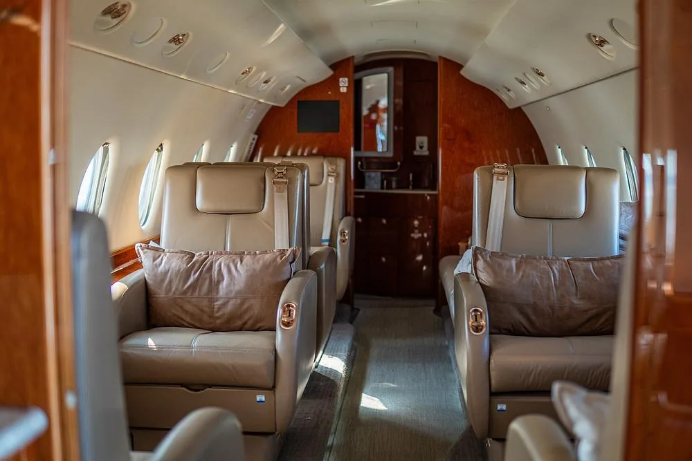 The luxurious interior cabin of a private jet features tan leather seats and dark wood paneling.
