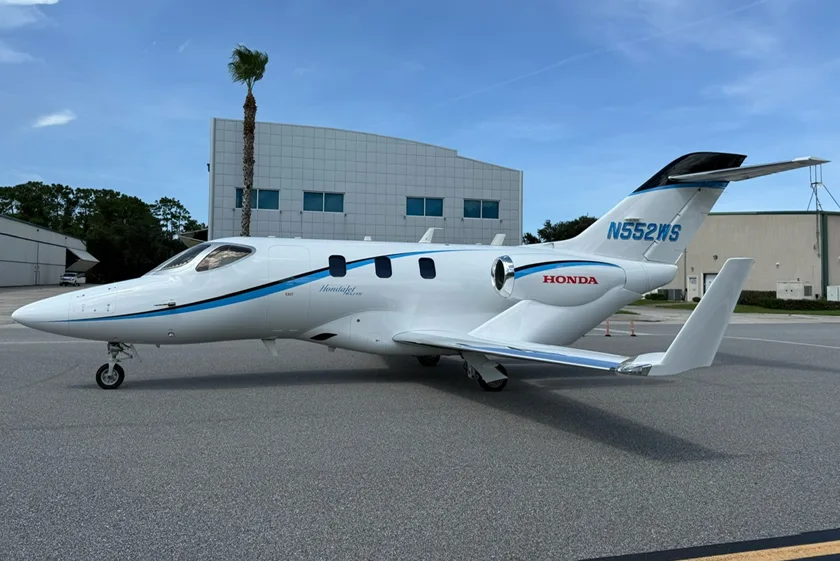A white and blue HondaJet (N552WS) is parked on an asphalt apron next to a building and a palm tree.