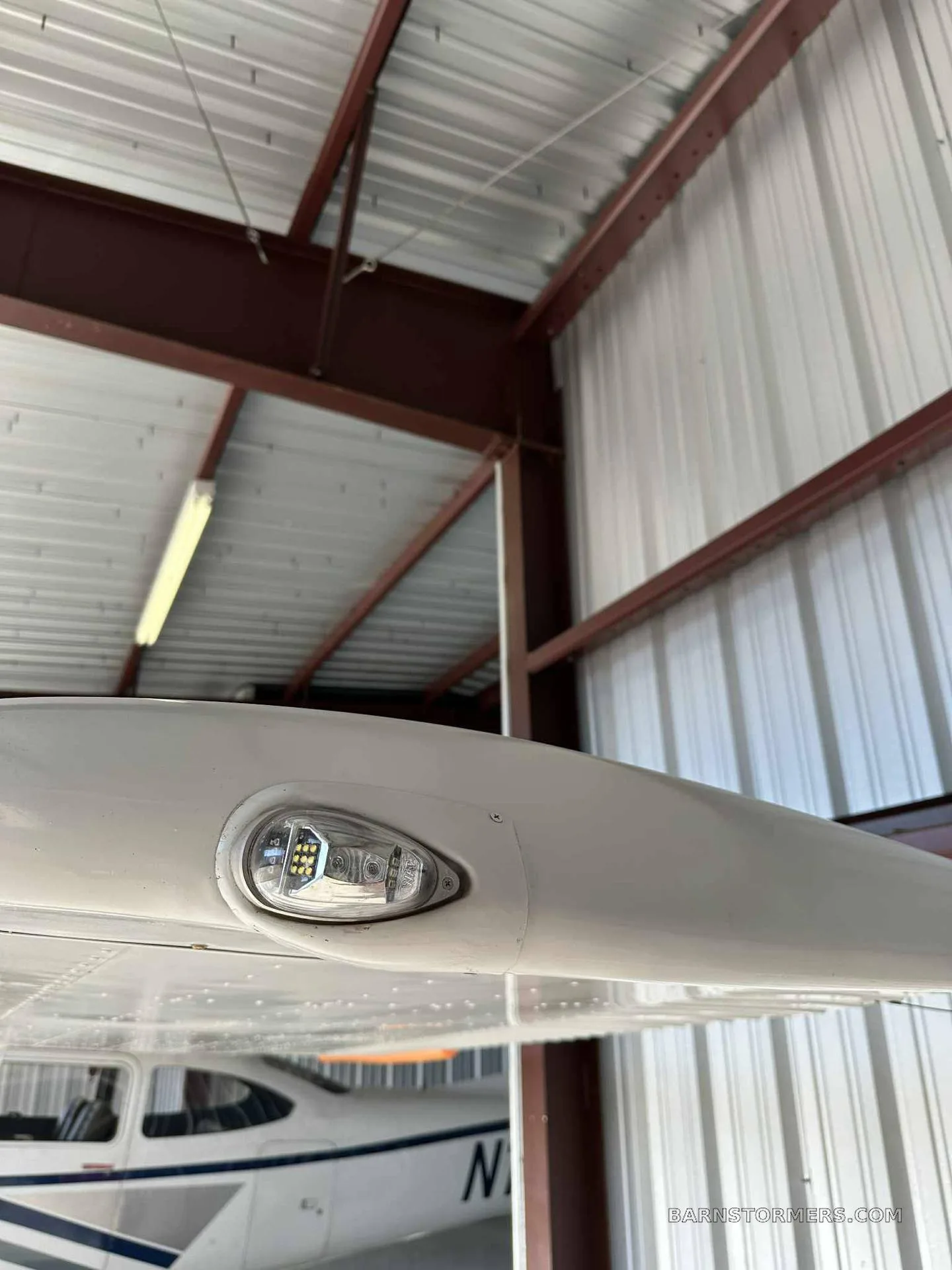 A close-up view of the LED wingtip light on a white aircraft, with the hangar roof visible above.