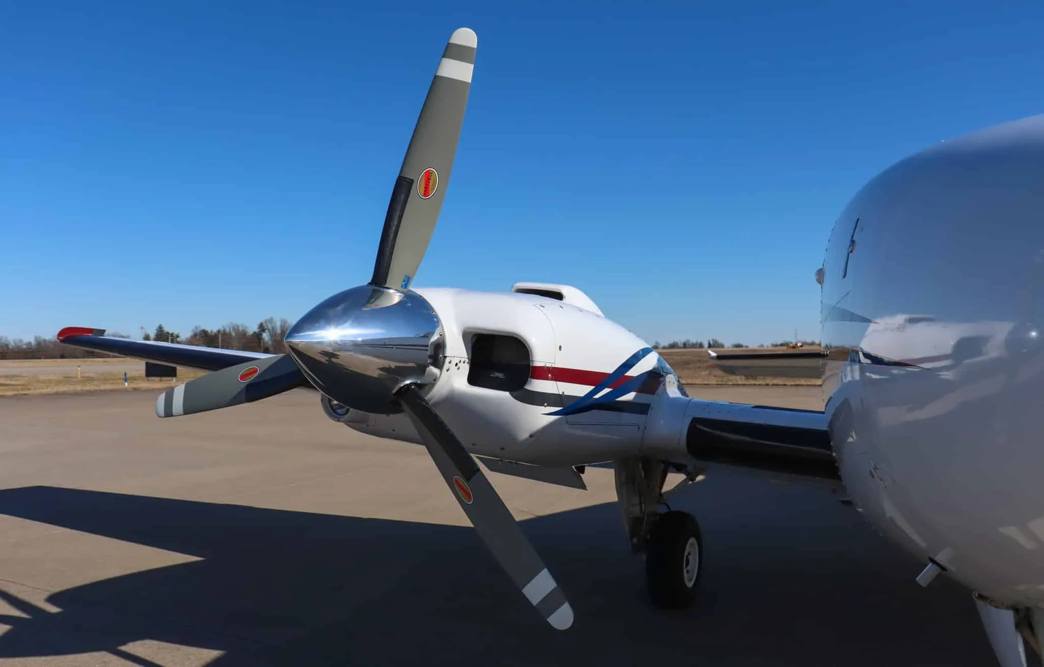 Close-up of the right engine and propeller of a white Beechcraft Baron N204G, showing the polished spinner and gray propeller blades.