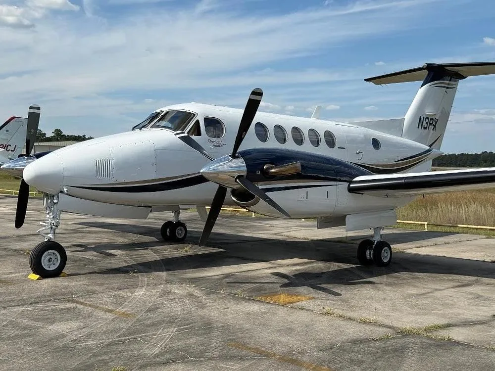 A white and dark blue Beechcraft King Air N3PX is parked on an tarmac under a partly cloudy sky.