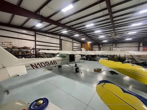 A white Cessna 150/152 type aircraft with registration N10946 is parked in a hangar, viewed from the left rear.