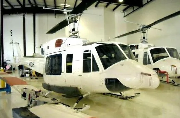 Two white Bell 212 helicopters, with N703H visible on the tail of the left one, are parked inside a hangar.