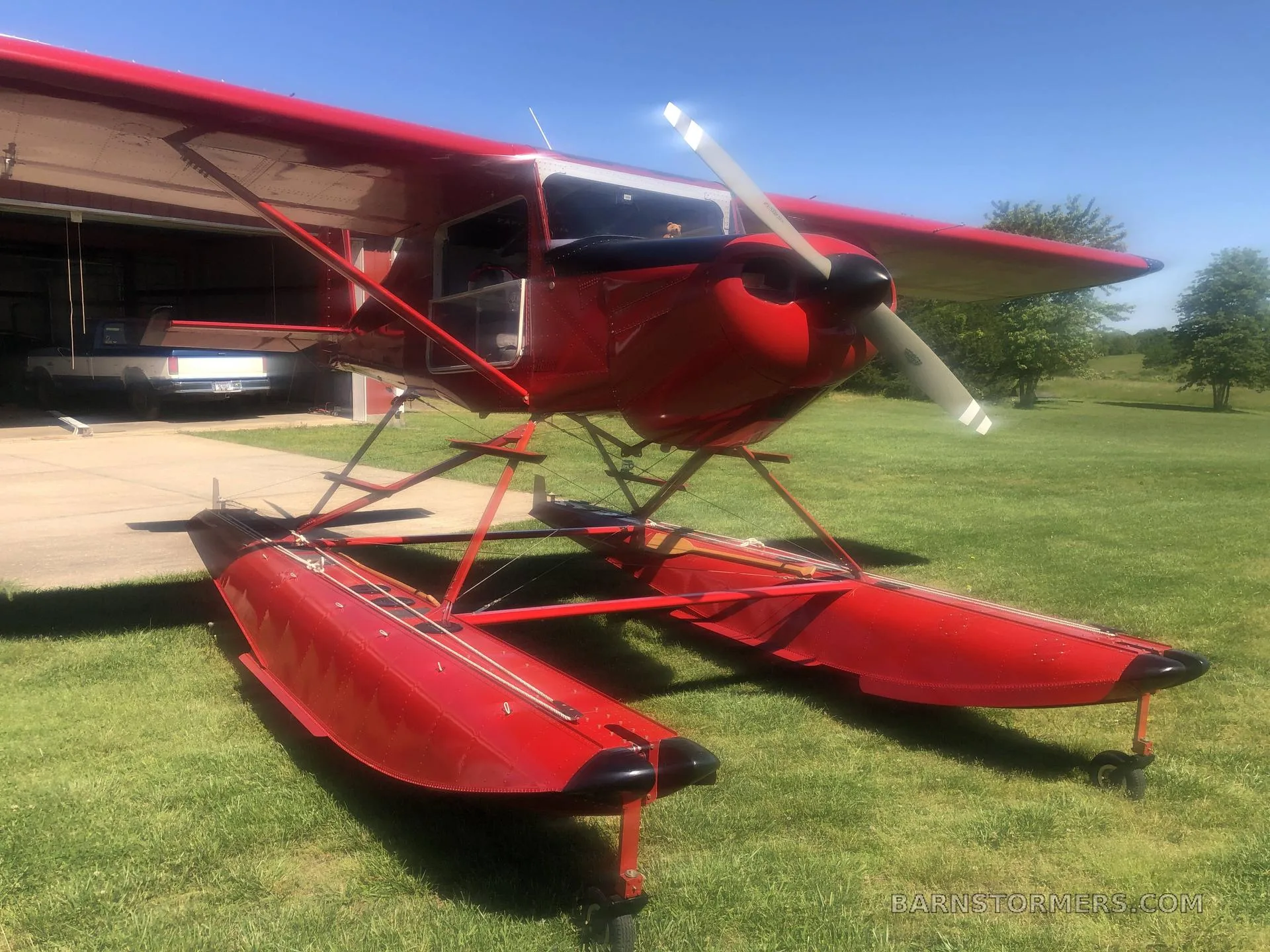A red floatplane with registration N11286 sits on green grass in front of an open hangar.
