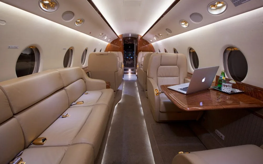 A luxurious aircraft cabin with tan leather seating, a sofa, and a table with a laptop.