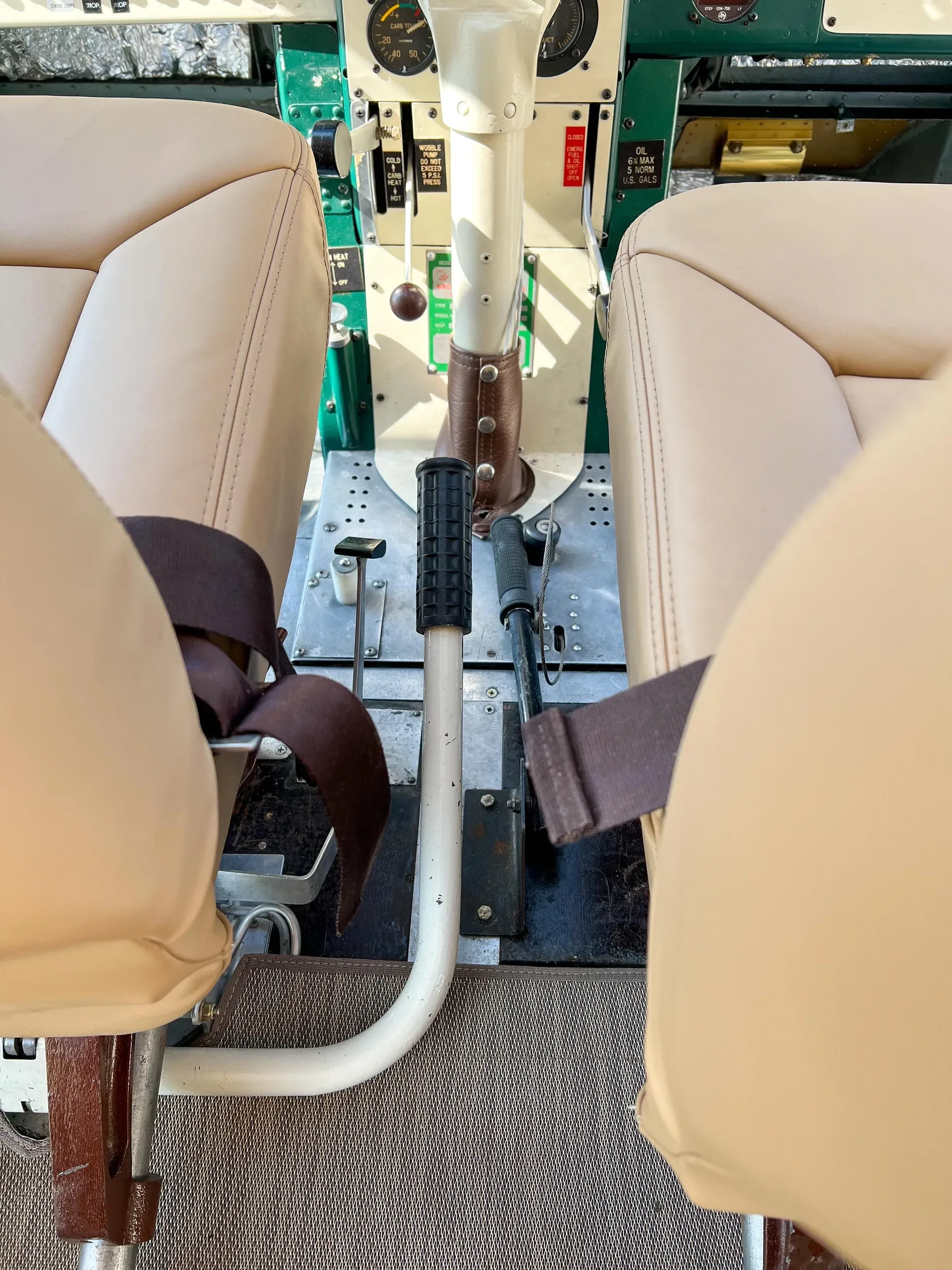 View of the aircraft's cockpit, showing the control column, pedals, and parts of the instrument panel between two tan seats.